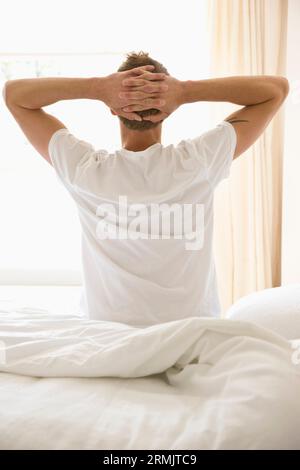 Junger Mann sitzt im Bett ausdehnen Stockfoto