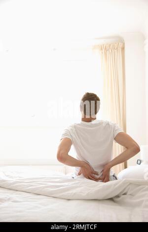 Junger Mann sitzt im Bett ausdehnen Stockfoto