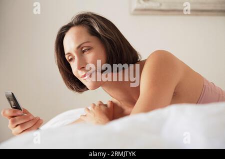 Frau, die Handy benutzt, lächelnd auf dem Bett liegt Stockfoto