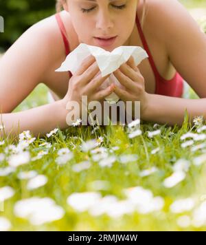 Junge Frau liegend auf Bauch auf dem Rasen Niesen Stockfoto
