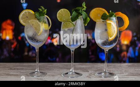 Drei Gläser Gin Tonic in Einer Strandbar bei Sonnenuntergang, mit Leuten im Hintergrund außerhalb des Blickwinkels. Stockfoto