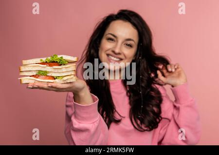 Fröhliche junge, schöne dunkelhaarige Frau, die ihre Lieblingssarnies vor der Kamera auf dem rosafarbenen Hintergrund zeigt. Gesundes Snackkonzept Stockfoto