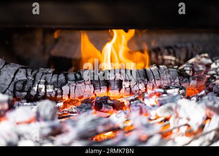 Grillgrube mit heißen Kohlen. Glühende und flammende Holzkohlegriketts für Feuergrill. Stockfoto