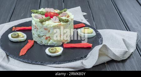 Schwarzer Schieferteller mit Ensaladilla rusa oder russischem Salat typisch spanische Tapa garniert mit roter Paprika, hart gekochtem Ei und Spargel Stockfoto