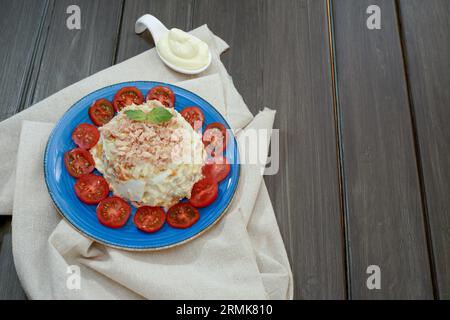 Ensaladilla rusa oder russischer Salat, typisch spanische Tapa mit Thunfisch und Mayonnaise auf blauem Teller mit Tomaten und grünen Blättern auf einer Raffia Stockfoto