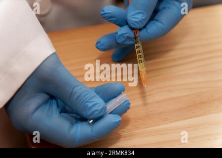 Arzthandschuhe in blauen Latexhandschuhen mit einer Spritze in der Hand auf dem Tisch in seiner Praxis Stockfoto