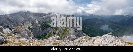 Panorama, Bergsteiger am Gipfel des Waxensteins, Blick über felsigen und schmalen Kamm des Waxensteins zum Eibsee und Hoellental mit Stockfoto