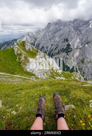 Füße einer Bergsteigerin mit Wanderschuhen, Blick auf bewölkte felsige Bergwelt mit Alpspitze, auf dem Schafsteig auf dem Waxenstein Stockfoto