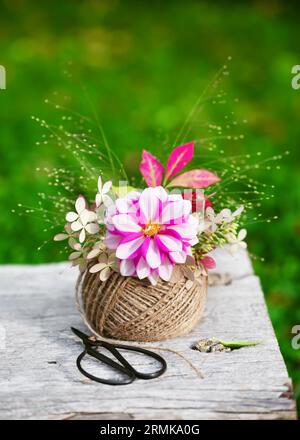 Wunderschöner Blumenstrauß mit rosa, weißen Dahlien, Hortensienblüten, Gras und Herbstfäden in einem Knäuel Jutegarn. Floristik- oder Gartenkonzept. Stockfoto