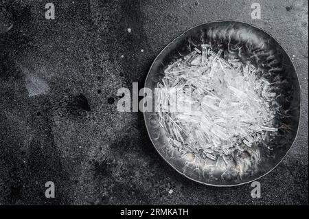 Menthol-Kristalle in einer Stahlkleingeschale. Schwarzer Hintergrund. Draufsicht. Leerzeichen kopieren. Stockfoto