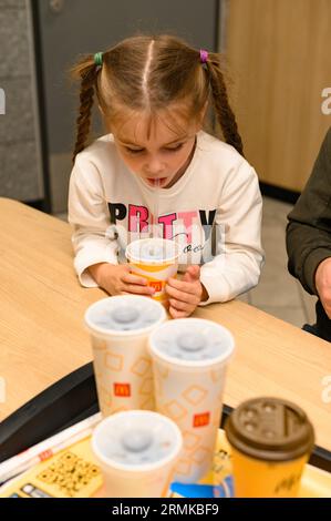 Ivano-Frankivsk, Ukraine, 7. Juni 2023: Ein kleines und süßes Mädchen trinkt Coca-Cola in McDonald's. Stockfoto