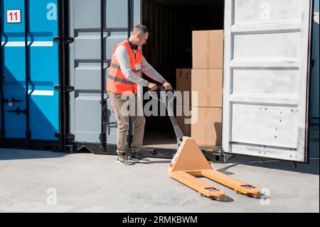 Vollschuss-Mann mit Palettenwagen Stockfoto