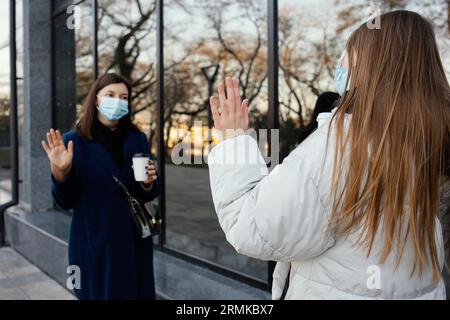 Freundinnen mit Masken winken Stockfoto