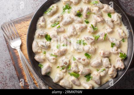 Zarte gedünstete Hühnerherzen in Knoblauchcremesauce mit Kräutern auf einem Teller auf dem Tisch. Horizontale Draufsicht von oben Stockfoto