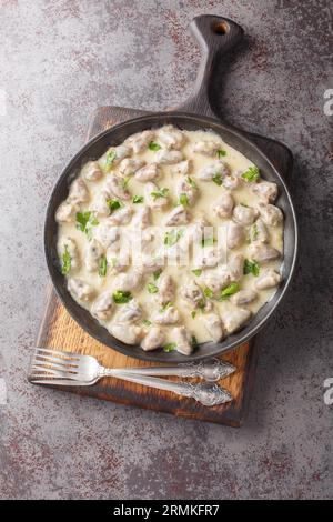 Hausgemachte Hühnerherzen in Knoblauch-Cremesauce aus nächster Nähe auf einem Teller auf dem Tisch. Vertikale Draufsicht von oben Stockfoto