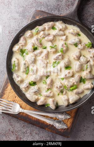 Köstliche Hühnerherzen in Knoblauch-Sahnesauce aus nächster Nähe auf einem Teller auf dem Tisch. Vertikale Draufsicht von oben Stockfoto