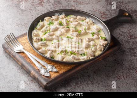 Gebratene und dann gedünstete Hühnerherzen in einer cremigen Sauce mit aromatischen Kräutern aus nächster Nähe auf einem Teller auf dem Tisch. Horizontal Stockfoto