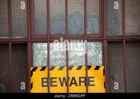 Ein gelb-schwarzes Schild auf dem vergitterten Fenster einer alten Fabrik Stockfoto