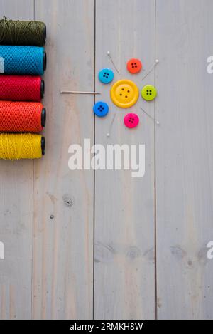 Bunte Garnspulen mit dekorativen Nadeln Stecknadeln bunte Knöpfe Holzschreibtisch Stockfoto