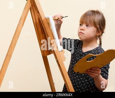 Seitenansicht Mädchen mit Down-Syndrom Malerei mit Staffelei Stockfoto
