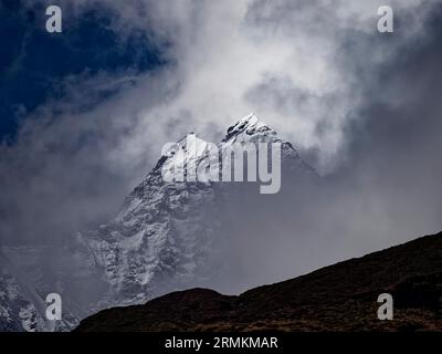 Zwei hell erleuchtete schneebedeckte Gipfel, die aus den Wolken hinter einem dunklen Bergrücken in der Annapurna-Region, Nepal, ragen Stockfoto