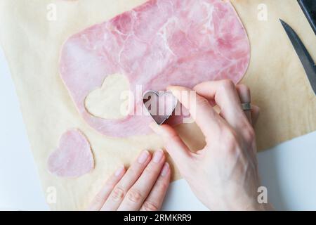 Der Koch schneidet herzförmigen Wurstschinken in Herzform auf Pergament, Draufsicht, Nahaufnahme. Pizza zum Valentinstag kochen Stockfoto