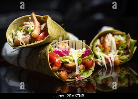 Hausgemachte vegane Tortillas mit roten Bohnen, Süßkartoffeln, Tomaten und Guacamole mit Saucen und Gewürzen auf schwarzem Hintergrund. Stockfoto