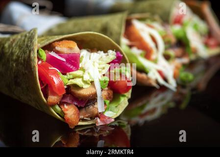 Hausgemachte vegane Tortillas mit roten Bohnen, Süßkartoffeln, Tomaten und Guacamole mit Saucen und Gewürzen auf schwarzem Hintergrund. Stockfoto