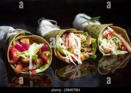 Hausgemachte vegane Tortillas mit roten Bohnen, Süßkartoffeln, Tomaten und Guacamole mit Saucen und Gewürzen auf schwarzem Hintergrund. Stockfoto