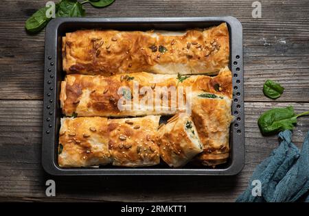 Frisch gebackener hausgemachter gerollter Kuchen mit Spinat in einem Backblech auf einem hölzernen Hintergrund. Draufsicht. Stockfoto