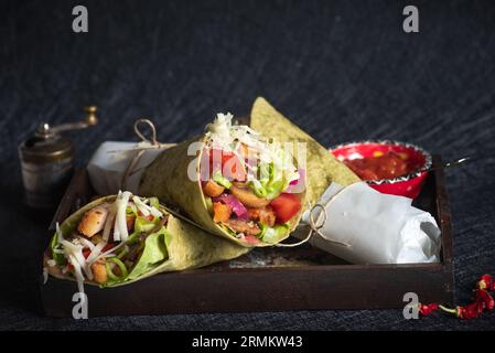 Hausgemachte vegane Tortillas mit roten Bohnen, Süßkartoffeln, Tomaten und Guacamole mit Saucen und Gewürzen auf schwarzem Hintergrund. Stockfoto