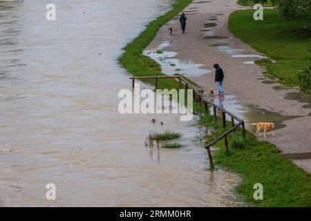 München, Deutschland. 29. August 2023. Passanten spazieren am Ufer der überfluteten Isar entlang, die durch die bayerische Hauptstadt fließt. Quelle: Peter Kneffel/dpa/Alamy Live News Stockfoto