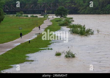 München, Deutschland. 29. August 2023. Passanten spazieren am Ufer der überfluteten Isar entlang, die durch die bayerische Hauptstadt fließt. Quelle: Peter Kneffel/dpa/Alamy Live News Stockfoto