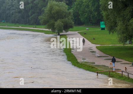 München, Deutschland. 29. August 2023. Passanten spazieren am Ufer der überfluteten Isar entlang, die durch die bayerische Hauptstadt fließt. Quelle: Peter Kneffel/dpa/Alamy Live News Stockfoto