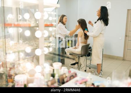 Remote-View-Gruppe von positiven weiblichen Make-up-Künstlern und Friseurinnen, die mit Models im Schönheitssalon arbeiten. Konzept von vierhändigem Make-up und Styling. Stockfoto