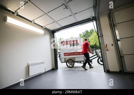 29. August 2023, Schleswig-Holstein, Lübeck: Matthias Jendrian, Fahrradlogistiker Lü-Bike, steigt bei der Eröffnung des ersten Mikrodepots in Lübeck vor einer Depot-Garage auf sein Lastenrad. Das Depot soll die Lübecker Altstadt vom Fracht- und Lieferverkehr entlasten. Foto: Christian Charisius/dpa Stockfoto