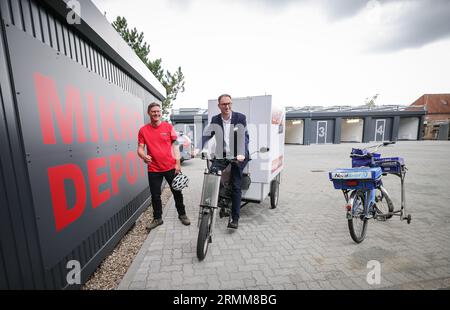 29. August 2023, Schleswig-Holstein, Lübeck: Jan Lindenau (SPD, r), Oberbürgermeister von Lübeck, sitzt bei der Eröffnung des ersten Mikrodepots in Lübeck auf einem Lü-Bike des Bike-Logistikspezialisten Matthias Jendrian (l). Das Depot soll die Lübecker Altstadt vom Fracht- und Lieferverkehr entlasten. Foto: Christian Charisius/dpa Stockfoto