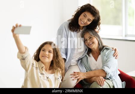 Fröhliche kaukasische Teenagerin, Erwachsene Mutter und ältere Großmutter machen Selfie auf dem Smartphone Stockfoto