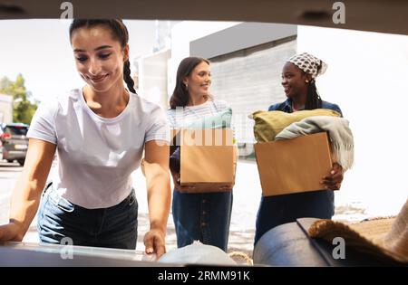 Drei junge Damen packen Auto mit Kartons voller Sachen Stockfoto