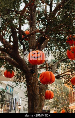 Heller Kürbis mit einem gruseligen Halloween-Gesicht, das an einem Baum mit Girlanden hängt. Hintergrund für halloween-Party Stockfoto