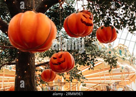 Heller Kürbis mit einem gruseligen Halloween-Gesicht, das an einem Baum mit Girlanden hängt. Hintergrund für Urlaubsposter Stockfoto