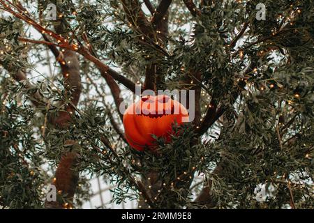 Heller Kürbis mit einem gruseligen Halloween-Gesicht, das an einem Baum mit Girlanden hängt. Hintergrund für halloween-Party Stockfoto