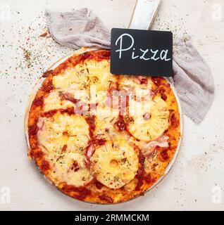 Tropische hawaiianische Pizza mit Ananasscheiben und Schinken auf einem Brett auf weißem Hintergrund, Draufsicht. Stockfoto