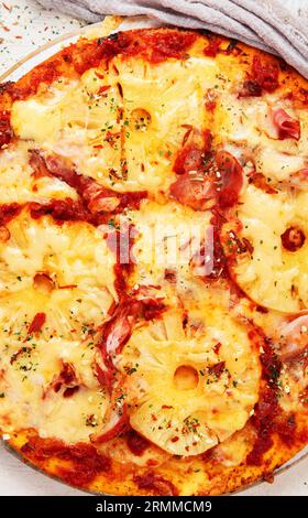 Tropische hawaiianische Pizza mit Ananasscheiben und Schinken auf einem Brett auf weißem Hintergrund, Draufsicht. Stockfoto