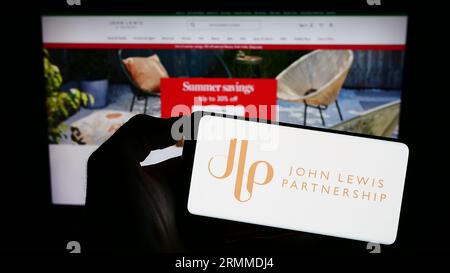 Person, die ein Mobiltelefon mit dem Logo des Einzelhandelsunternehmens John Lewis Partnership plc auf dem Bildschirm vor der Webseite hält. Konzentrieren Sie sich auf das Display des Telefons. Stockfoto