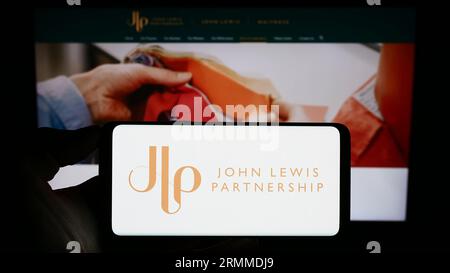 Person, die ein Mobiltelefon mit dem Logo des Einzelhandelsunternehmens John Lewis Partnership plc auf dem Bildschirm vor der Geschäftswebseite hält. Konzentrieren Sie sich auf das Display des Telefons. Stockfoto