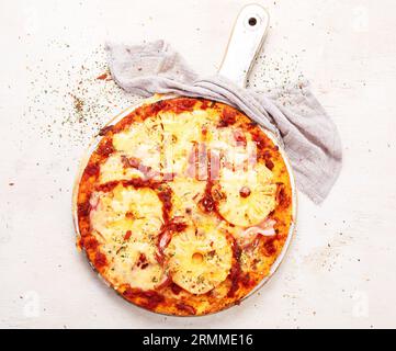 Tropische hawaiianische Pizza mit Ananasscheiben und Schinken auf einem Brett auf weißem Hintergrund, Draufsicht. Stockfoto