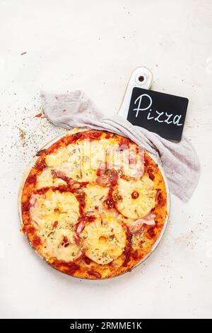 Tropische hawaiianische Pizza mit Ananasscheiben und Schinken auf einem Brett auf weißem Hintergrund, Draufsicht. Stockfoto