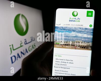 Person mit Mobiltelefon und Website des emiratischen Erdölunternehmens Dana Gas PJSC auf dem Bildschirm vor dem Logo. Konzentrieren Sie sich auf die Mitte der Telefonanzeige. Stockfoto