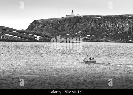 Schwarz-weiß-Foto Eines kleinen norwegischen Fischerboots, das Vardø verlässt, den hölzernen Leuchtturm von Vardø auf den Klippen des Meeres. Norwegen 7. Mai 2023 Stockfoto